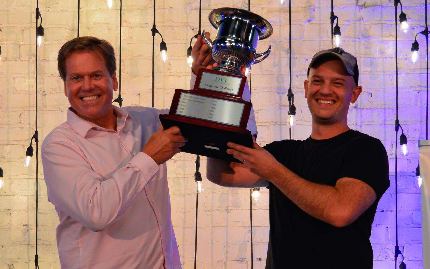 The 2022 Corporate Ping Pong Champions, Tom & Corey Hammerton from OSF, hoist the championship cup above their heads.